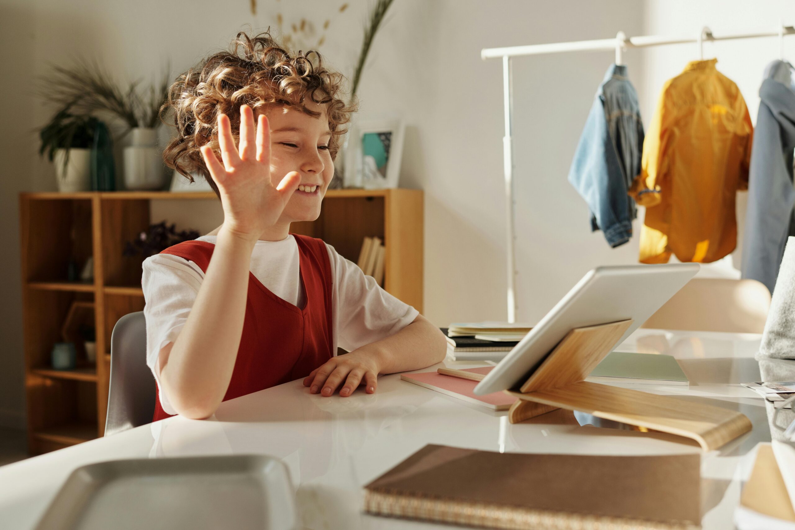 Happy child waving during an online learning session at home.