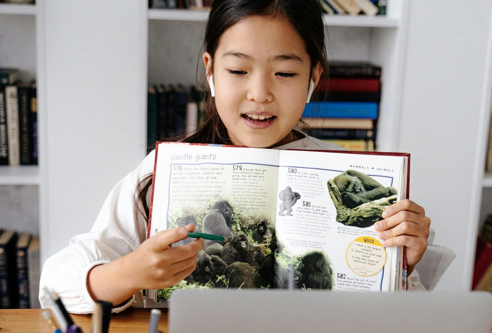 Girl studying online with a laptop and book, illustrating virtual education.