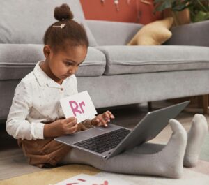 Child using laptop for online learning with alphabet cards at home.